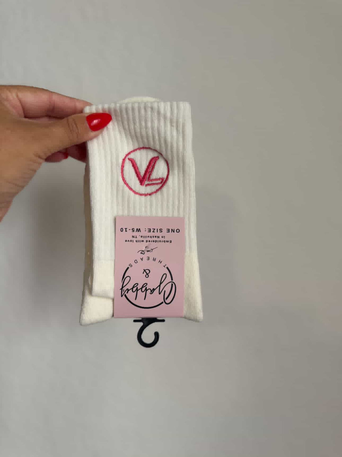 A picture of white grip socks with a custom pink logo for a pilates studio against a white wall