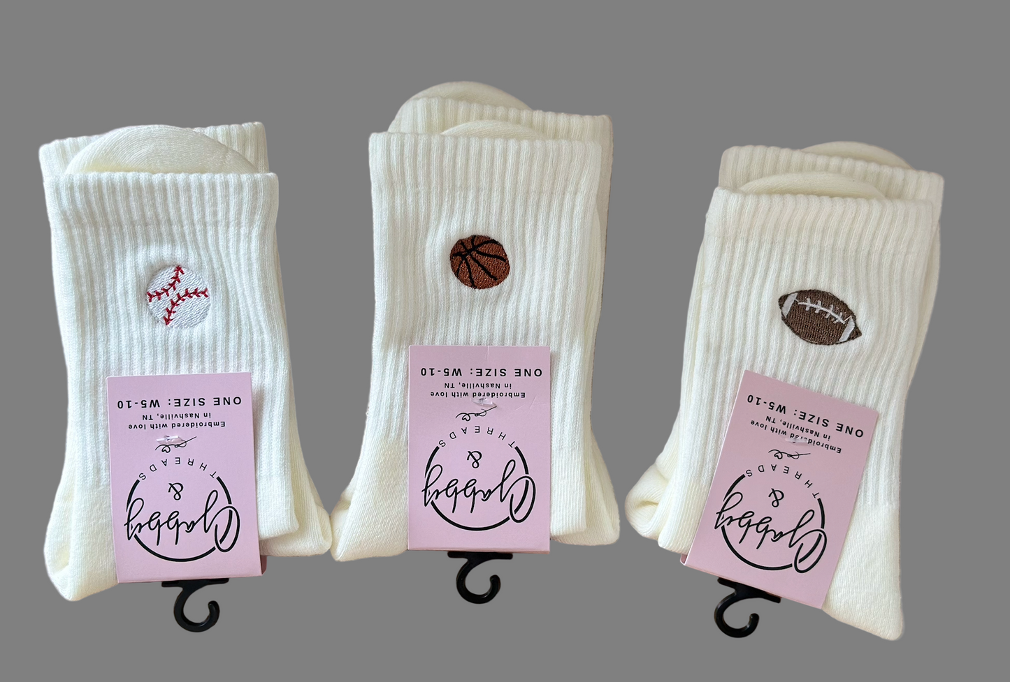Three pairs of socks on a wooden surface with different embroidered icons (baseball, football and a basketball)