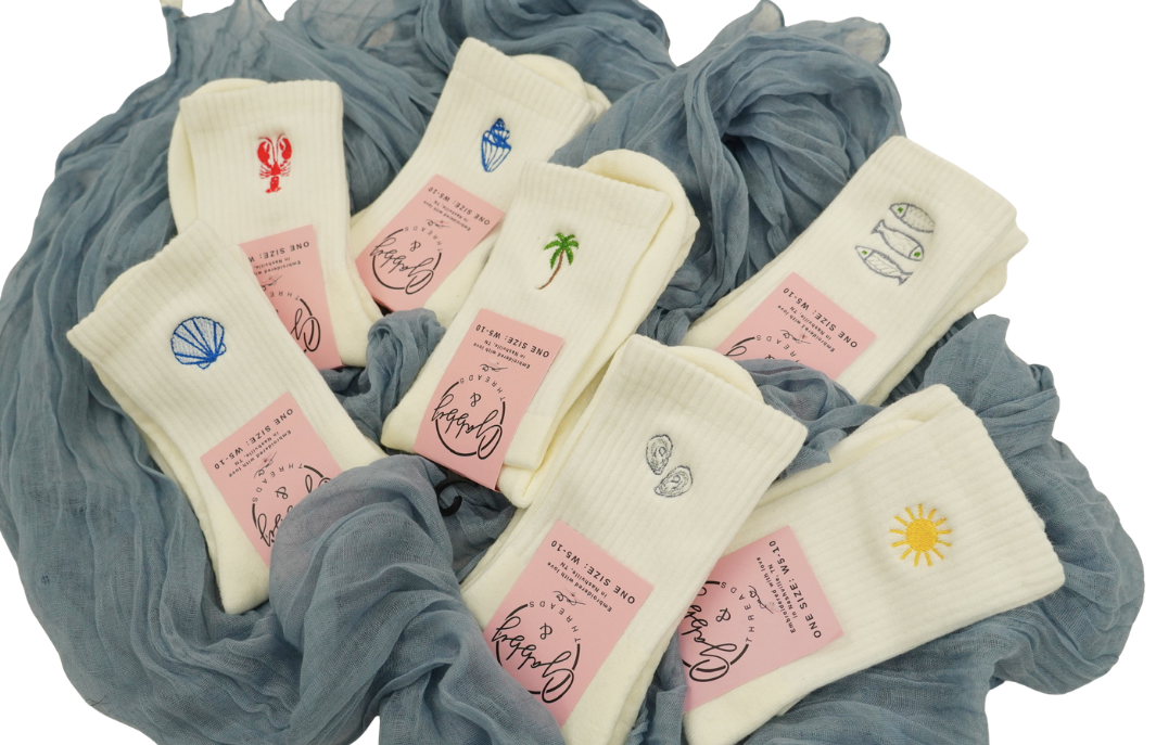 a bunch of pairs of white grip socks with different coastal icons embroidered on them lay on a blue towel