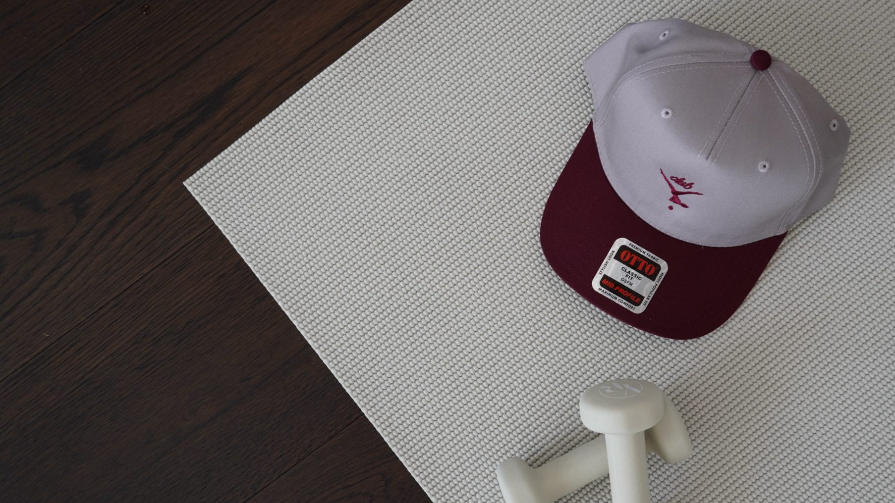 White cap with red brim and logo on a white mat, with a cream weights nearby.