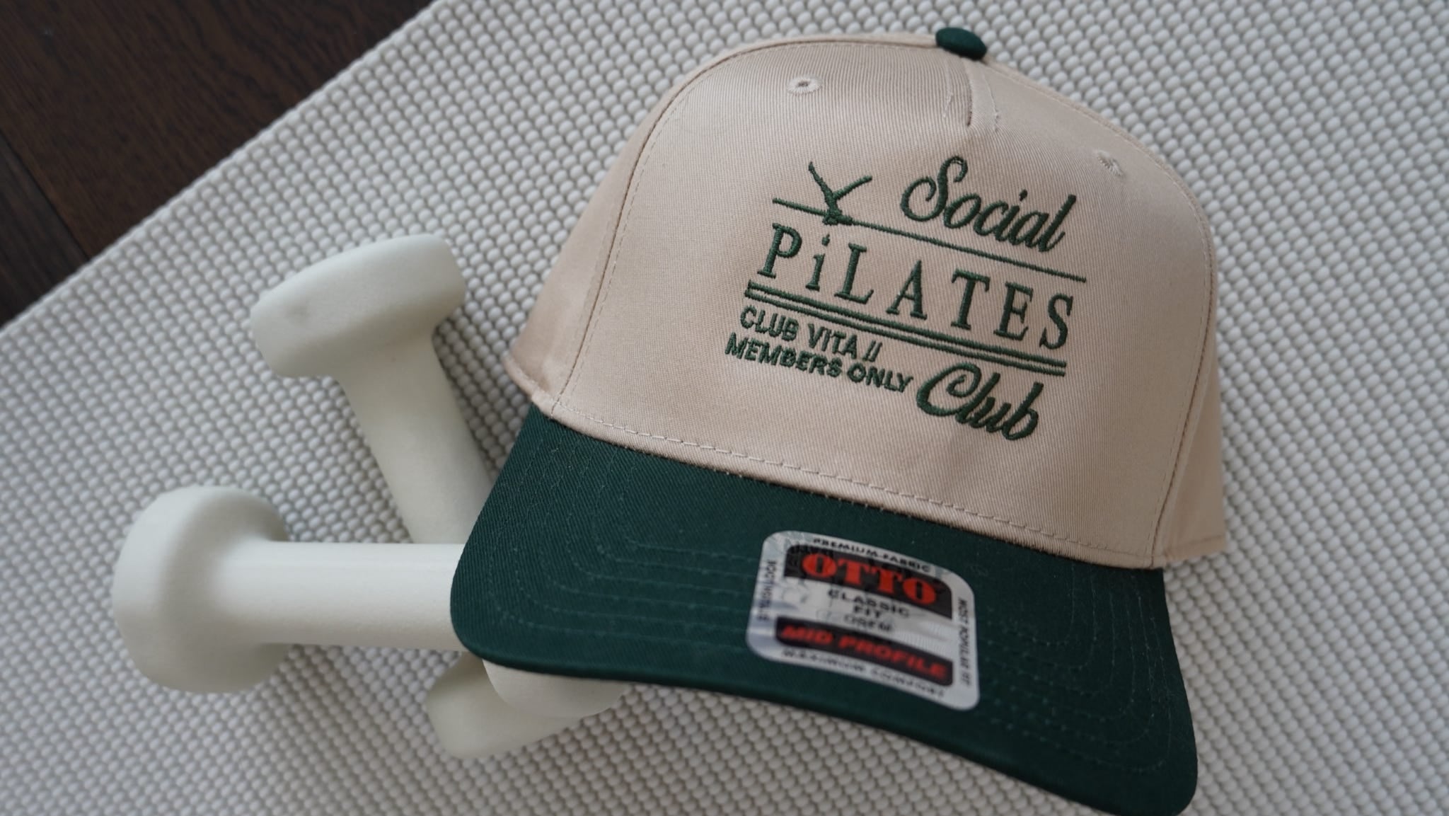 Beige and green cap with 'Social Pilates Club' text on a white mat