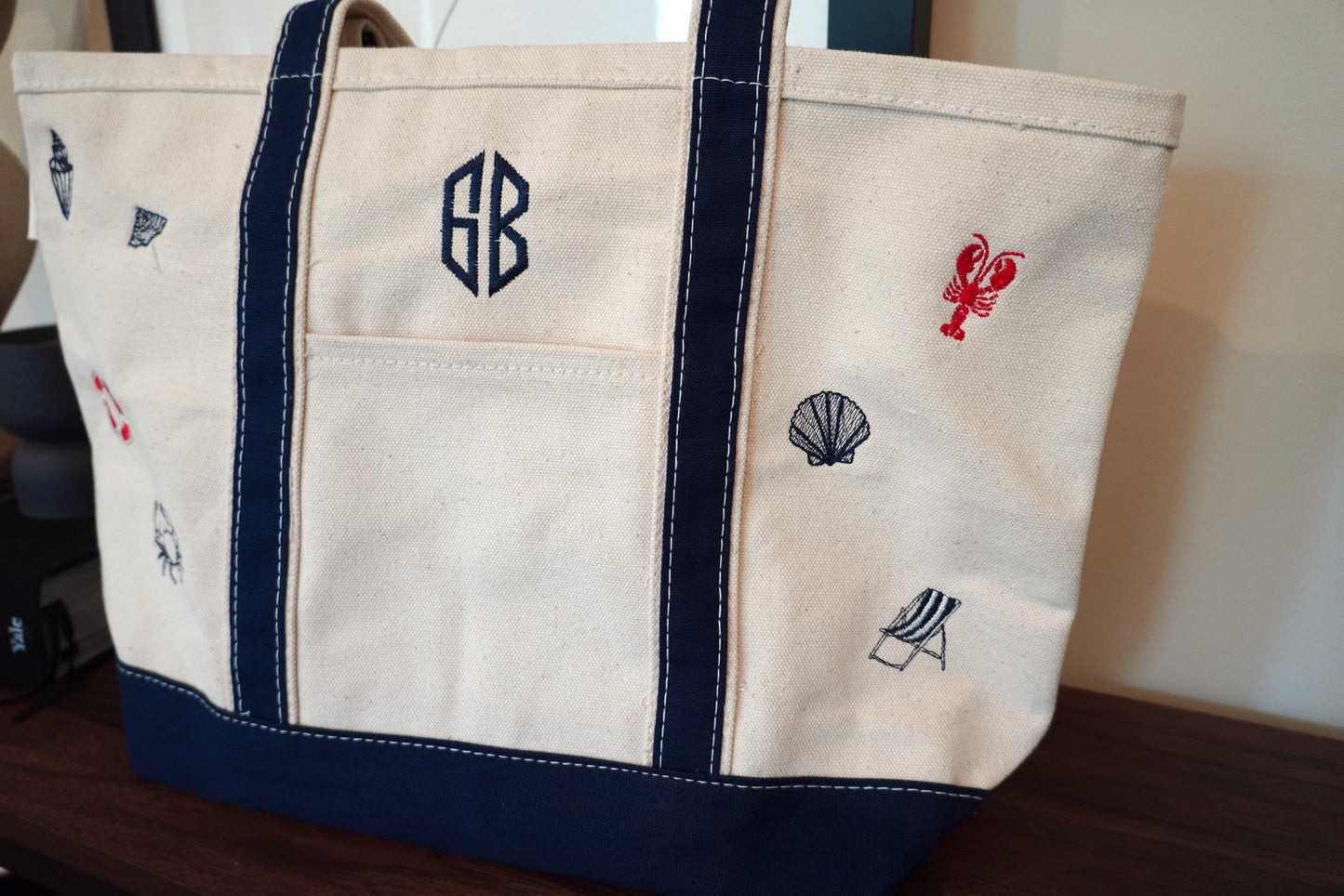 Beige tote bag with navy accents and coastal embroidered designs on a wooden surface