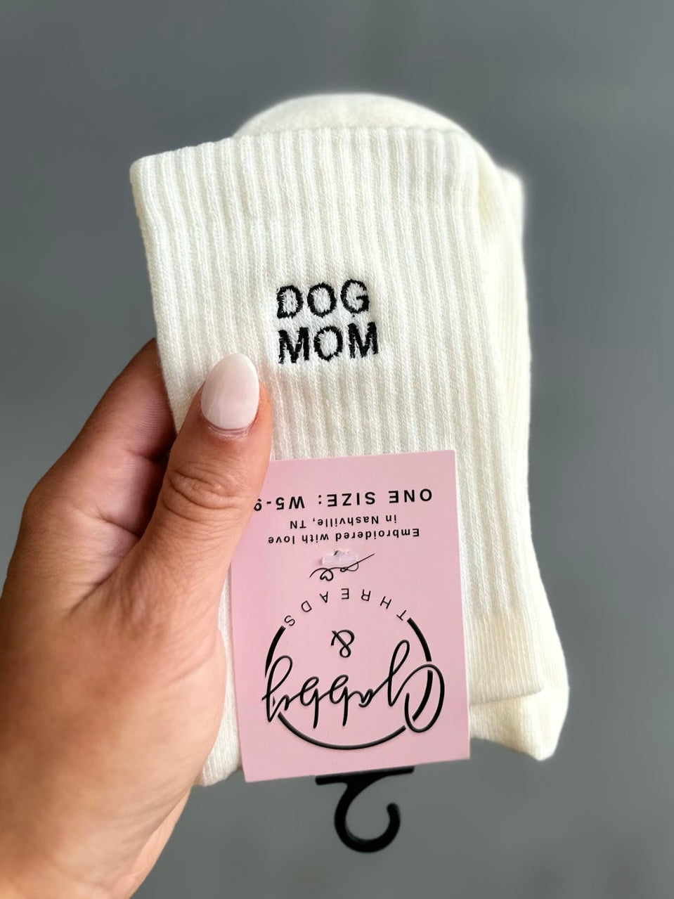 White socks with 'DOG MOM' text held by a hand against a gray background