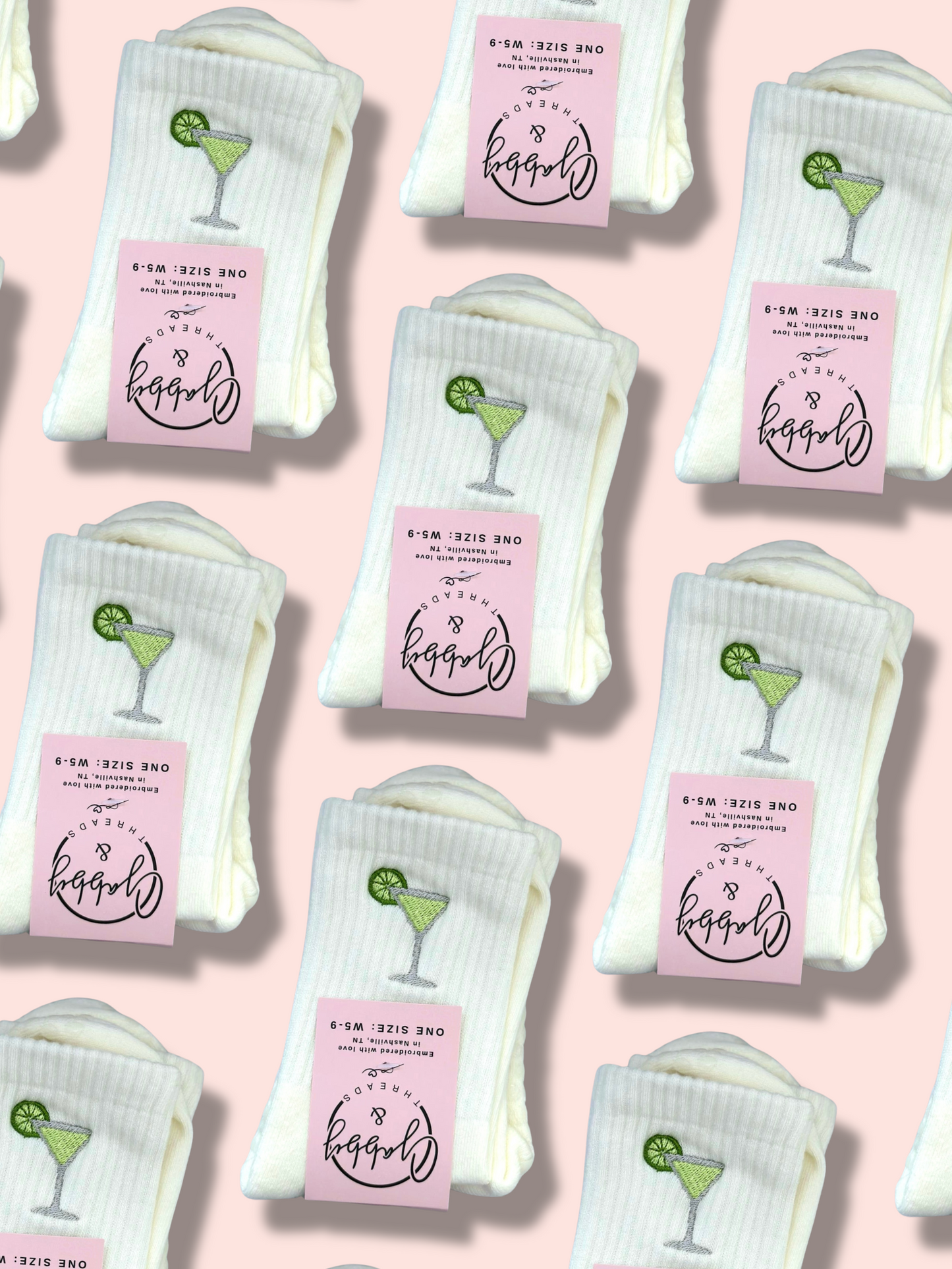 Pairs of white grip socks with green margaritas embroidered on them and 'Gabby & Threads' labels on a light pink background