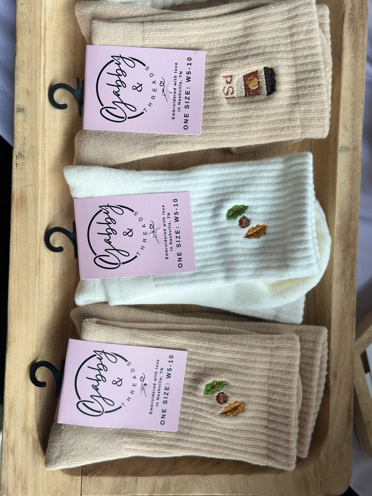 Three pairs of socks with embroidered designs on a wooden tray, each with a matching label.