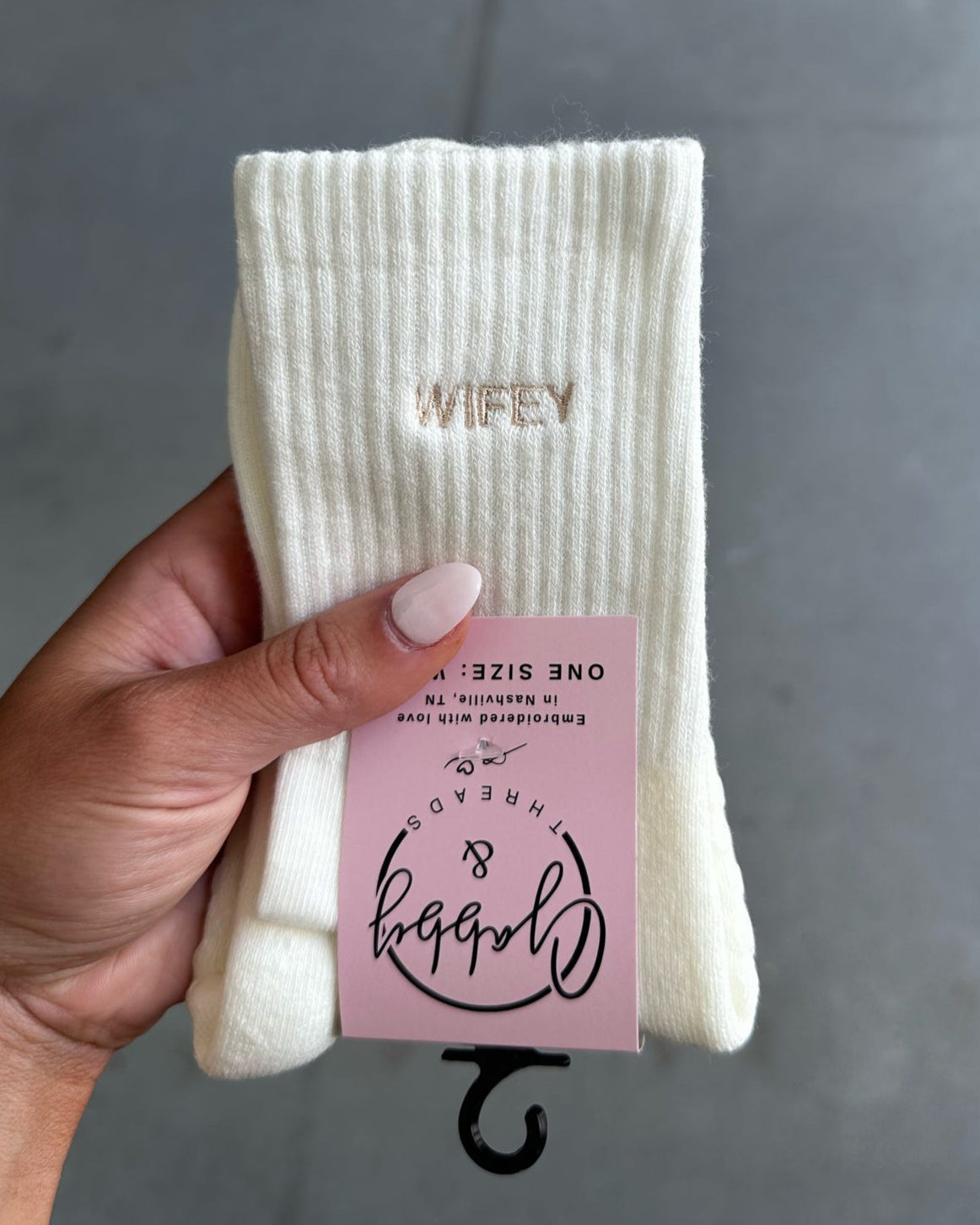 White grip sock with 'WIFEY' text held by a hand on a gray tiled floor.