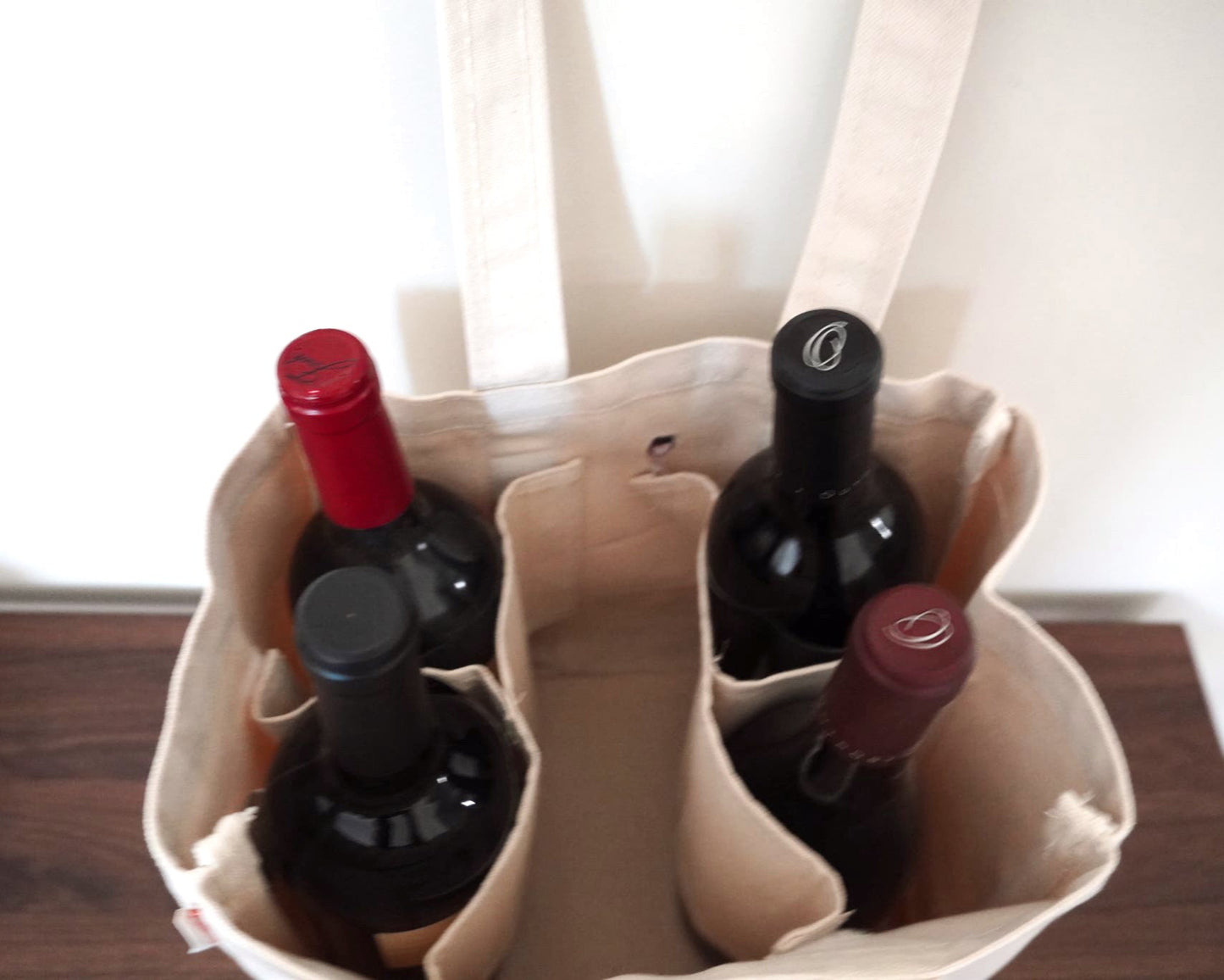 Four wine bottles in a beige tote bag on a wooden surface with a blurred background