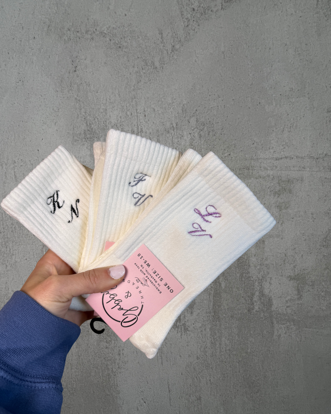 three pairs of white socks with initials embroidered on them