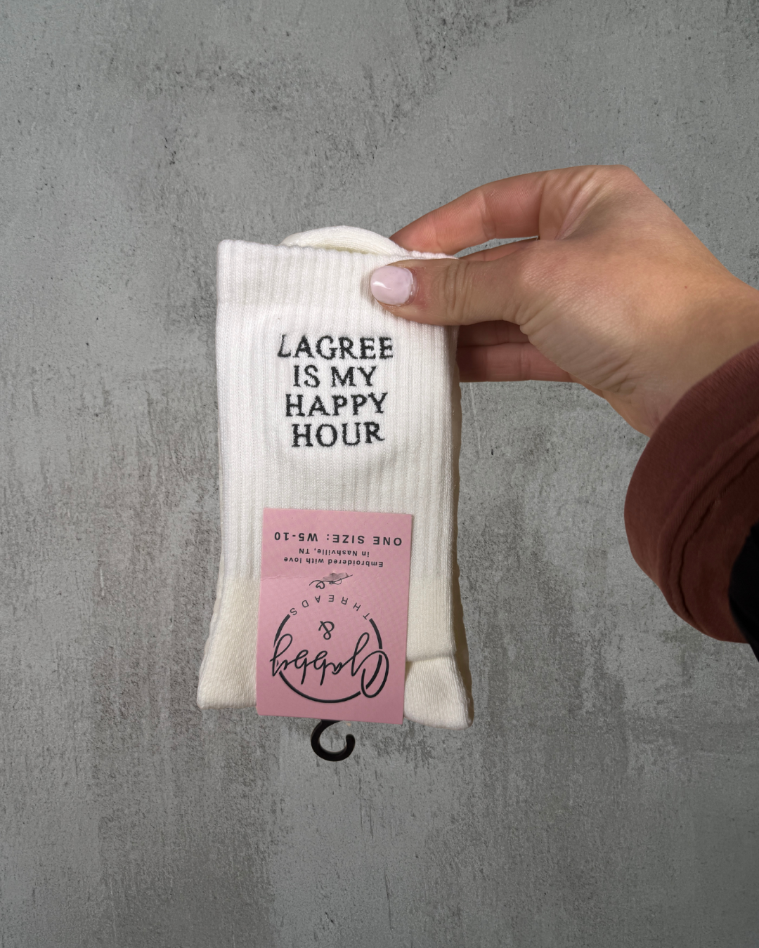 A pair of white embroidered socks that say "LAGREE IS MY HAPPY HOUR" embroidered in black