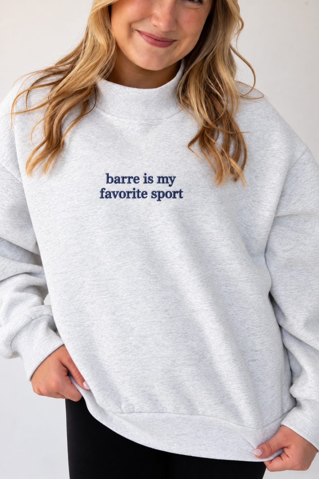 a model is wearing a heather gray mockneck sweatshirt with the words "barre is my favorite sport" embroidered on it 