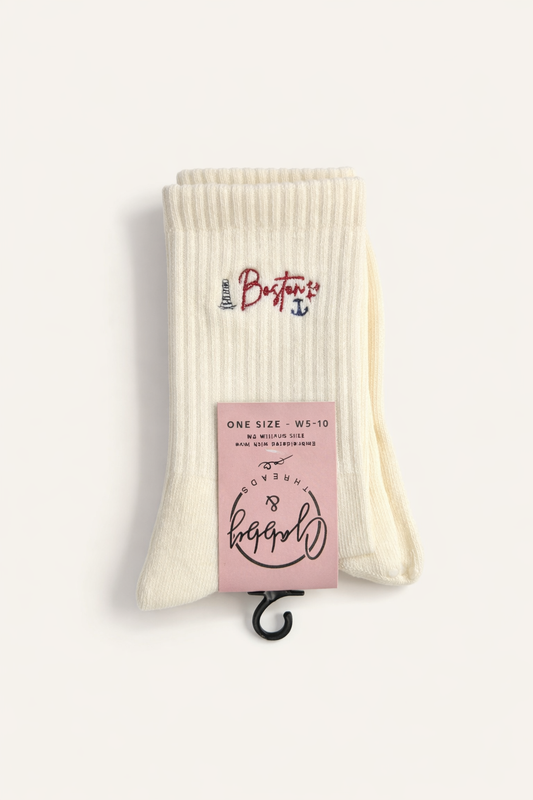 Pair of socks with a pink packaging label on a white background. the socks feature the word "Boston" and include icons that align with the city of boston