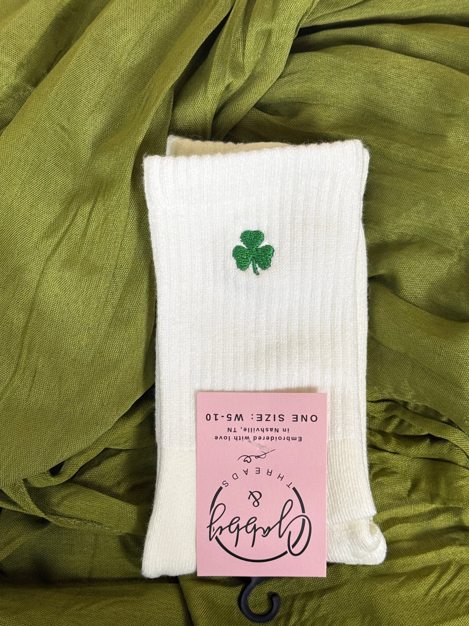 White grip socks for pilates with an embroidered clover for St. Patricks day against a green background