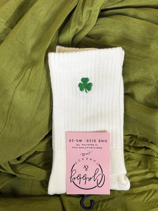 White grip socks for pilates with an embroidered clover for St. Patricks day against a green background