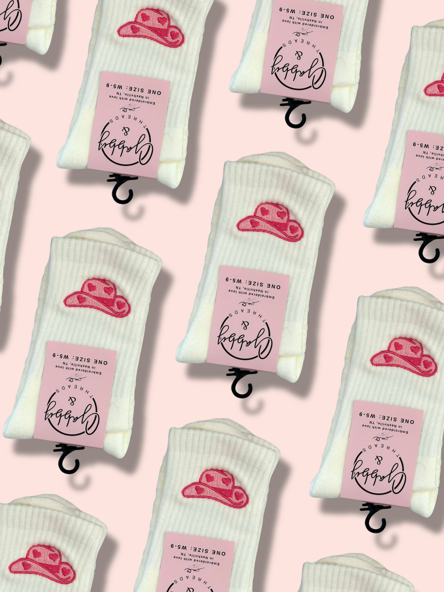 White socks with pink labels and pink cowgirl hat designs on a pink background