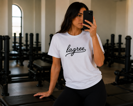 a women is standing in a lagree studio wearing a tshirt with the words "lagree" embroidered on it 