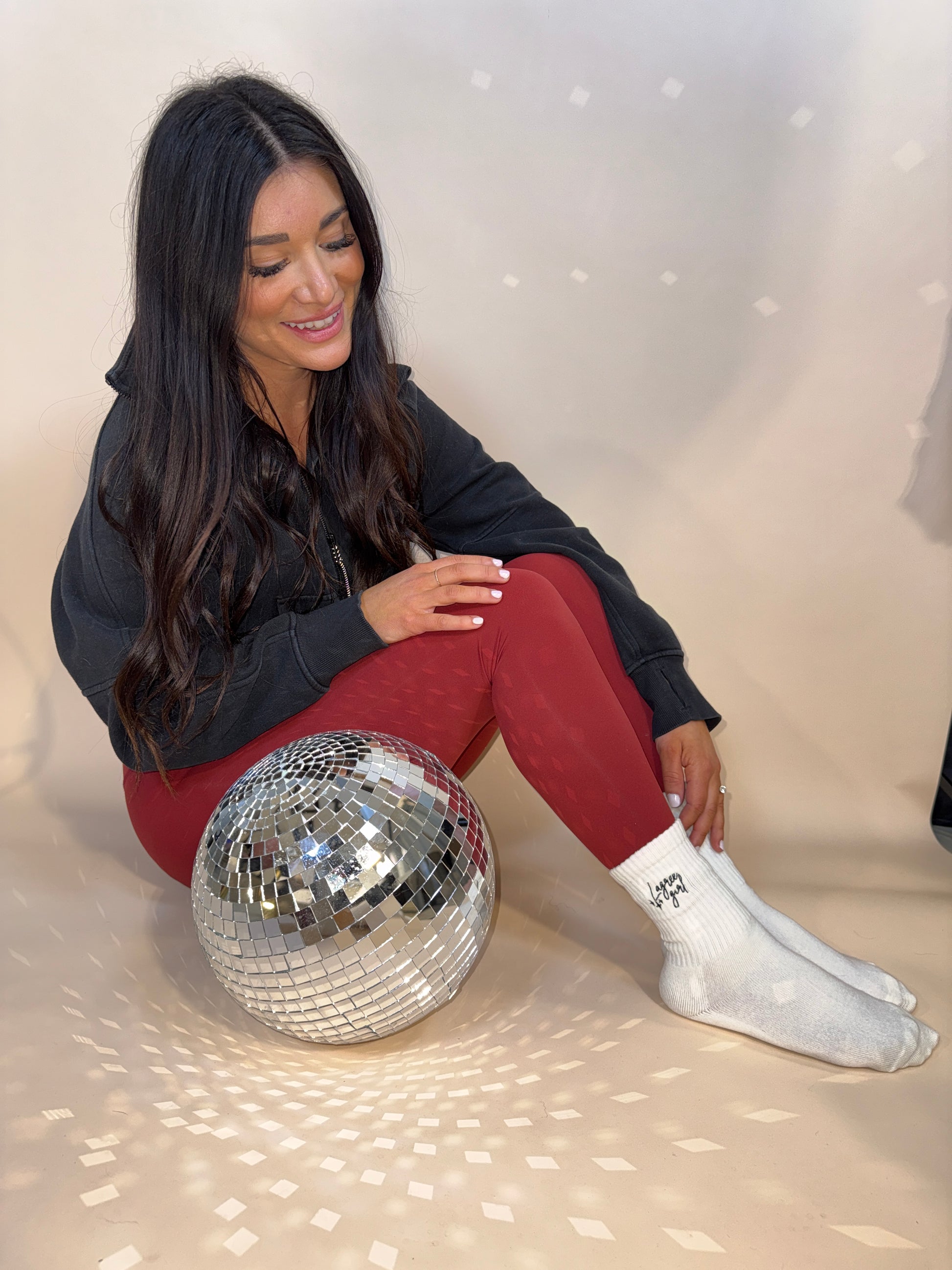 A girl is sitting next to a disco ball with a pair of pilates grip socks that say "Lagree Girl"