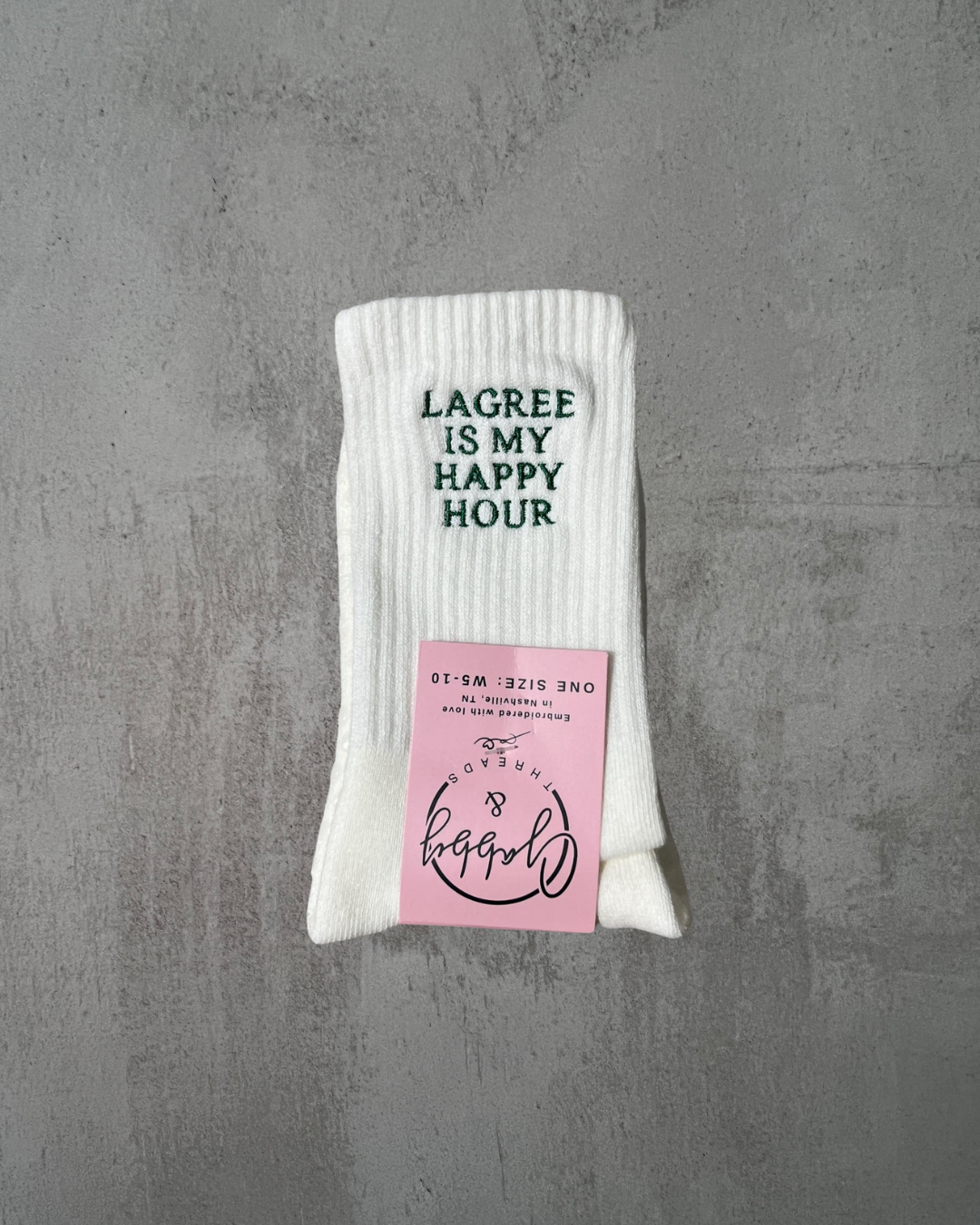 A pair of white embroidered socks that say "LAGREE IS MY HAPPY HOUR" embroidered in green. 