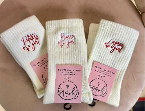Three pairs of white grip socks with the words "pilates girl" "lagree girl" and "barre girl" embroidered on them