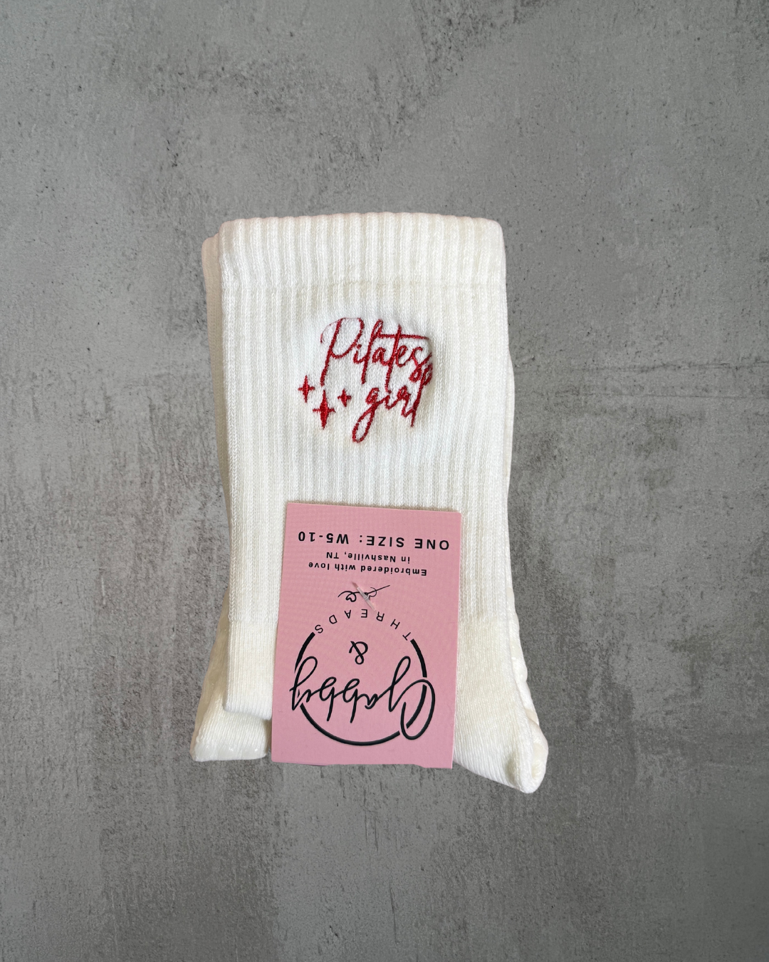 a pair of white grip socks with the words "pilates girl" embroidered on them 
