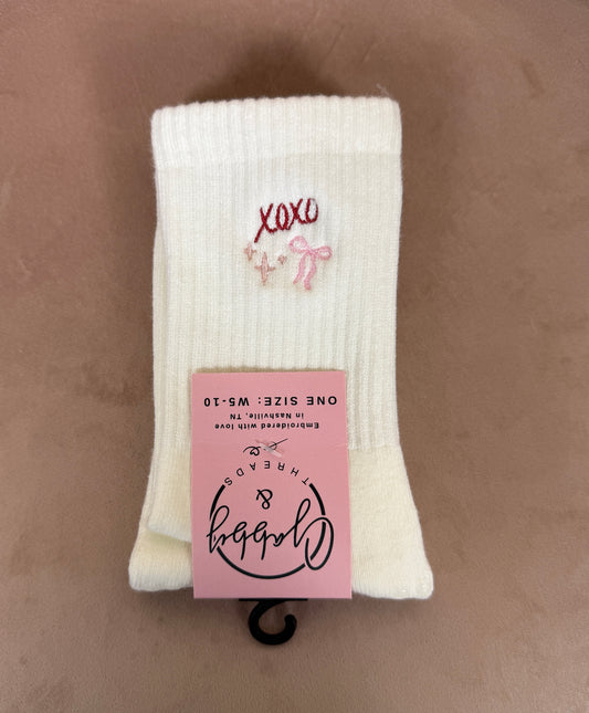 a pair of white grip socks with "xoxo," a pink bow and pink sparkles 
