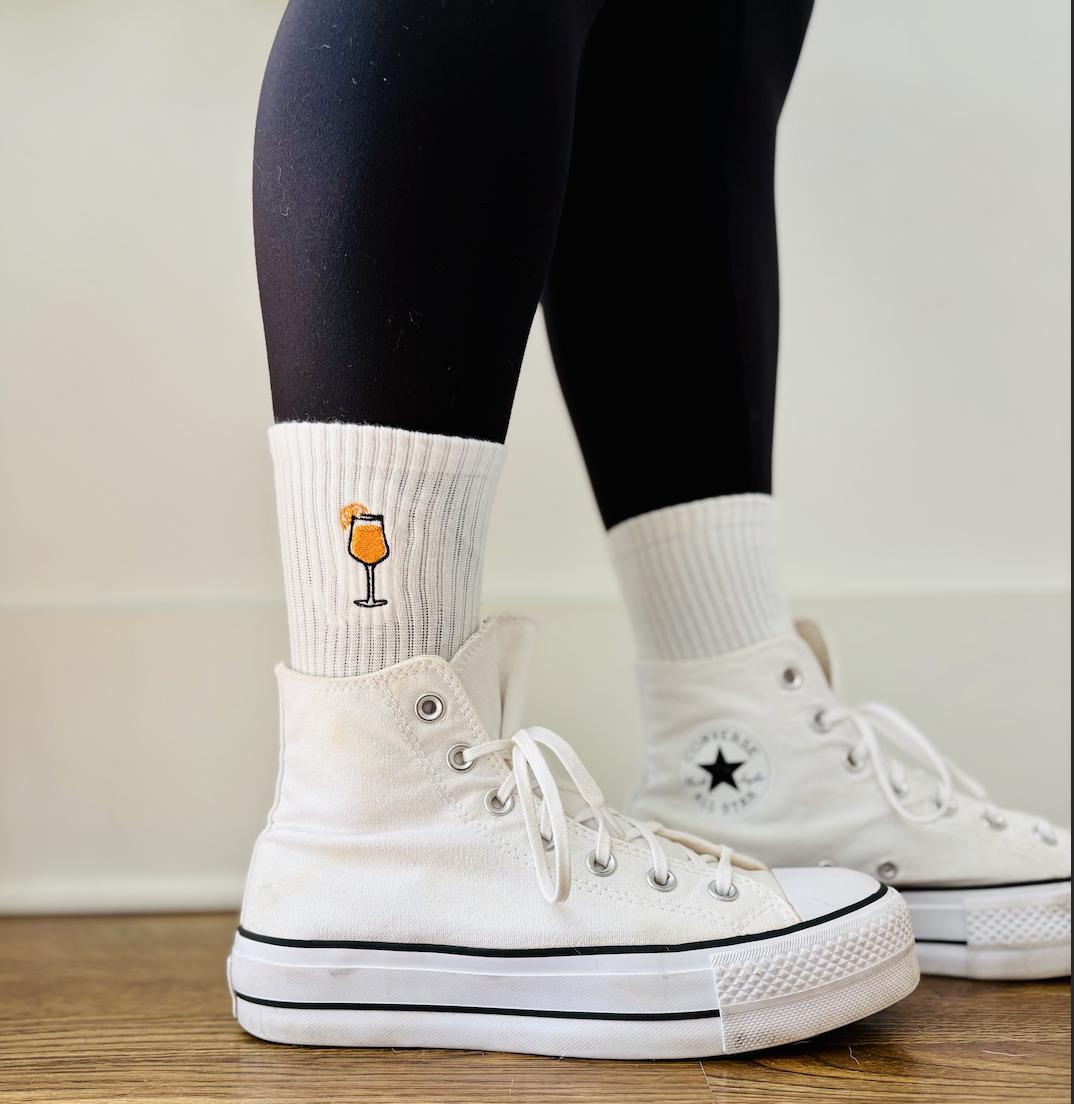 A person is wearing converse with aperol spritz embroidered crew socks