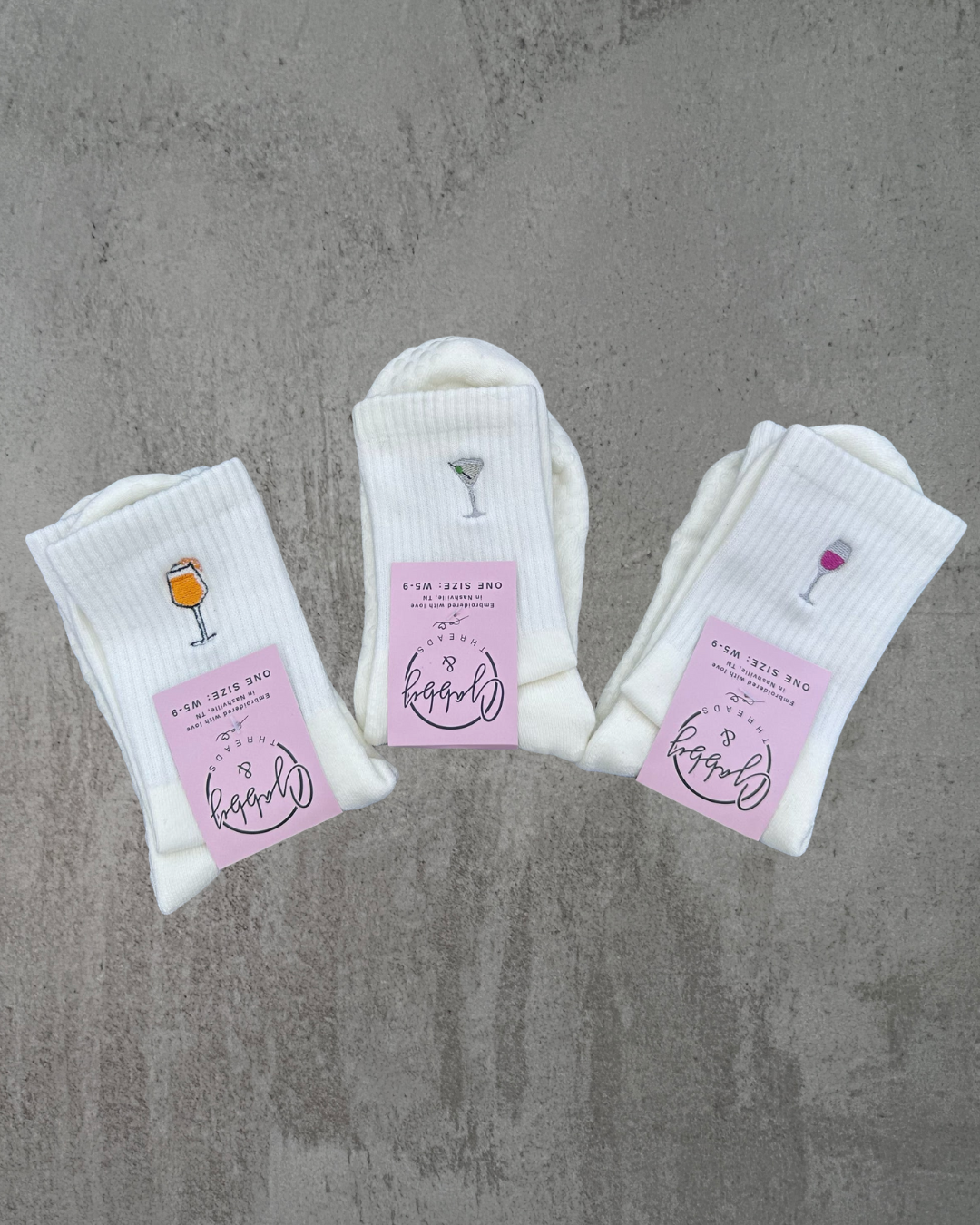 three pairs of white grip socks with different embroidered icons on them against a grey background 