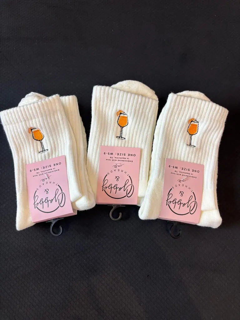 three pairs of embroidered aperol spritz socks are laying on a black yoga mat