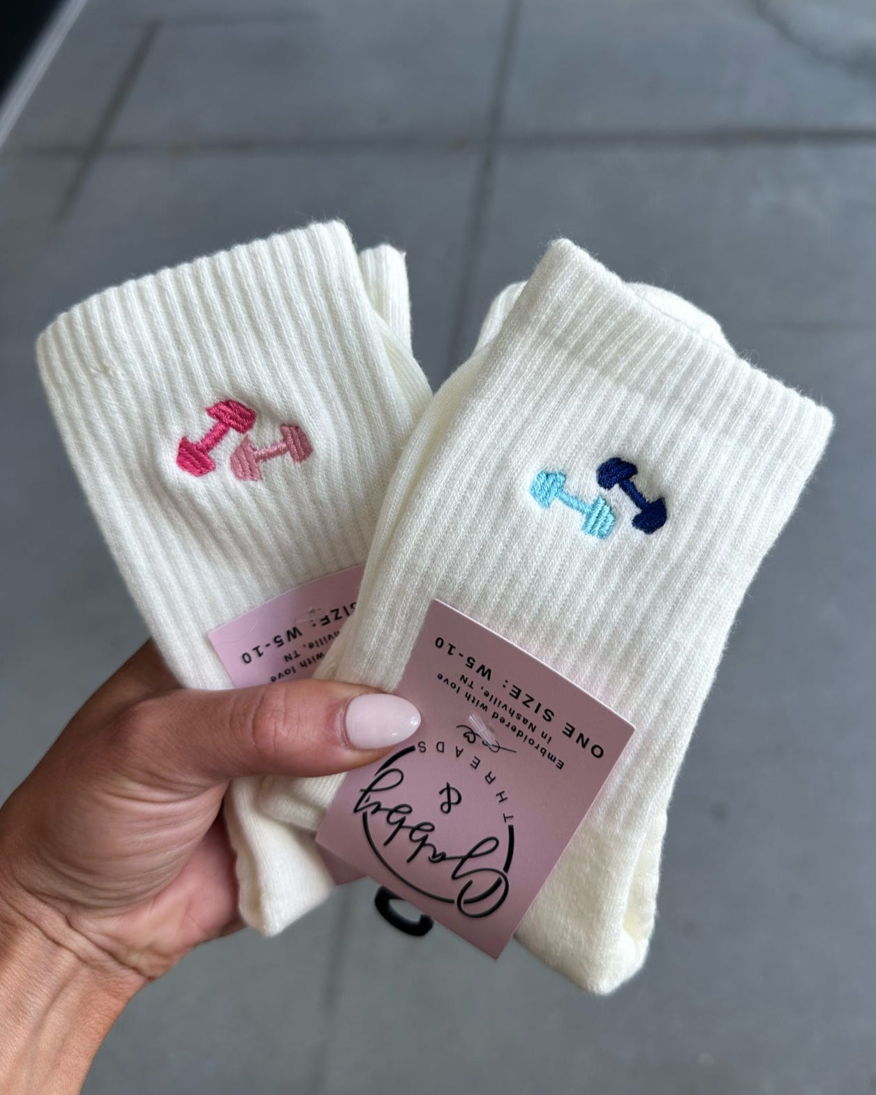 White grip socks with barbells held by a hand above a grey floor.