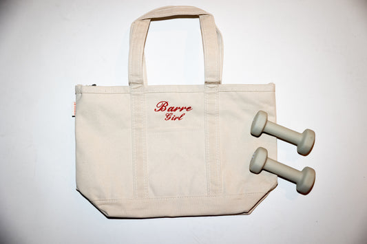 a canvas tote bag with the words "Barre Girl" embroidered on it lays against a white background next to two dumbbells