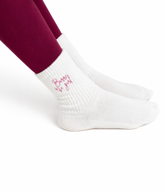 a person wearing maroon leggings wears a pair of white grip socks that say "Barre Girl" on them