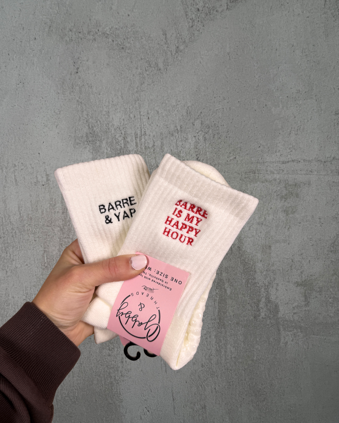 two pairs of white grip socks with different barre themed phrases embroidered on them