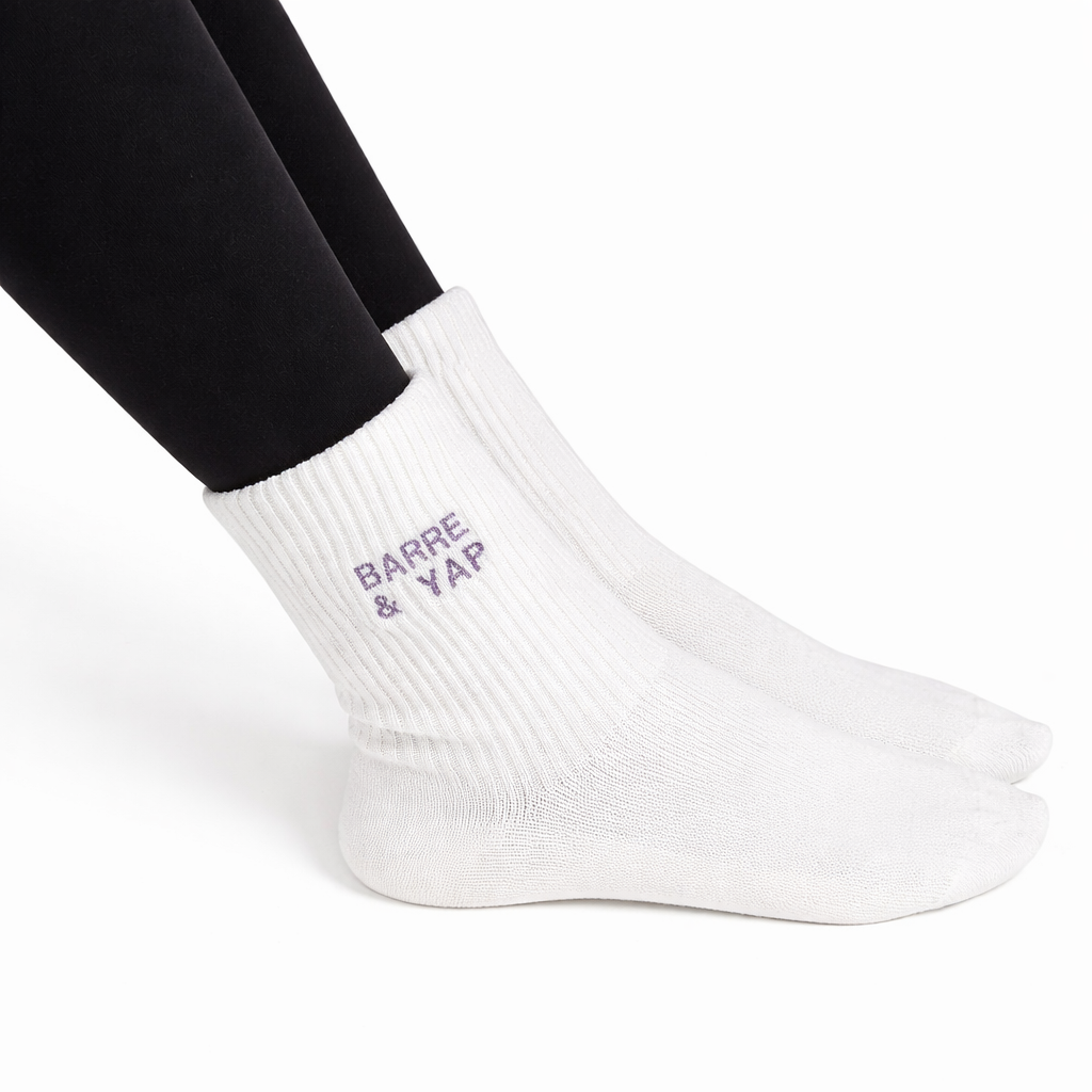 a person is wearing a pair of black leggings and a pair of white grip socks that say "barre & yap"