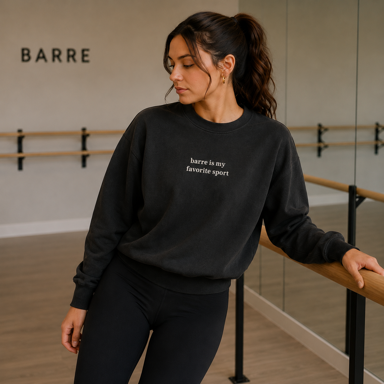 Woman in a black sweatshirt with 'barre is my favorite sport' text in a barre studio.