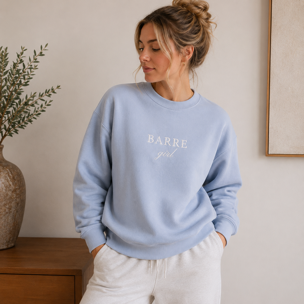Woman wearing a light blue sweatshirt with 'BARRE girl' text, standing indoors.