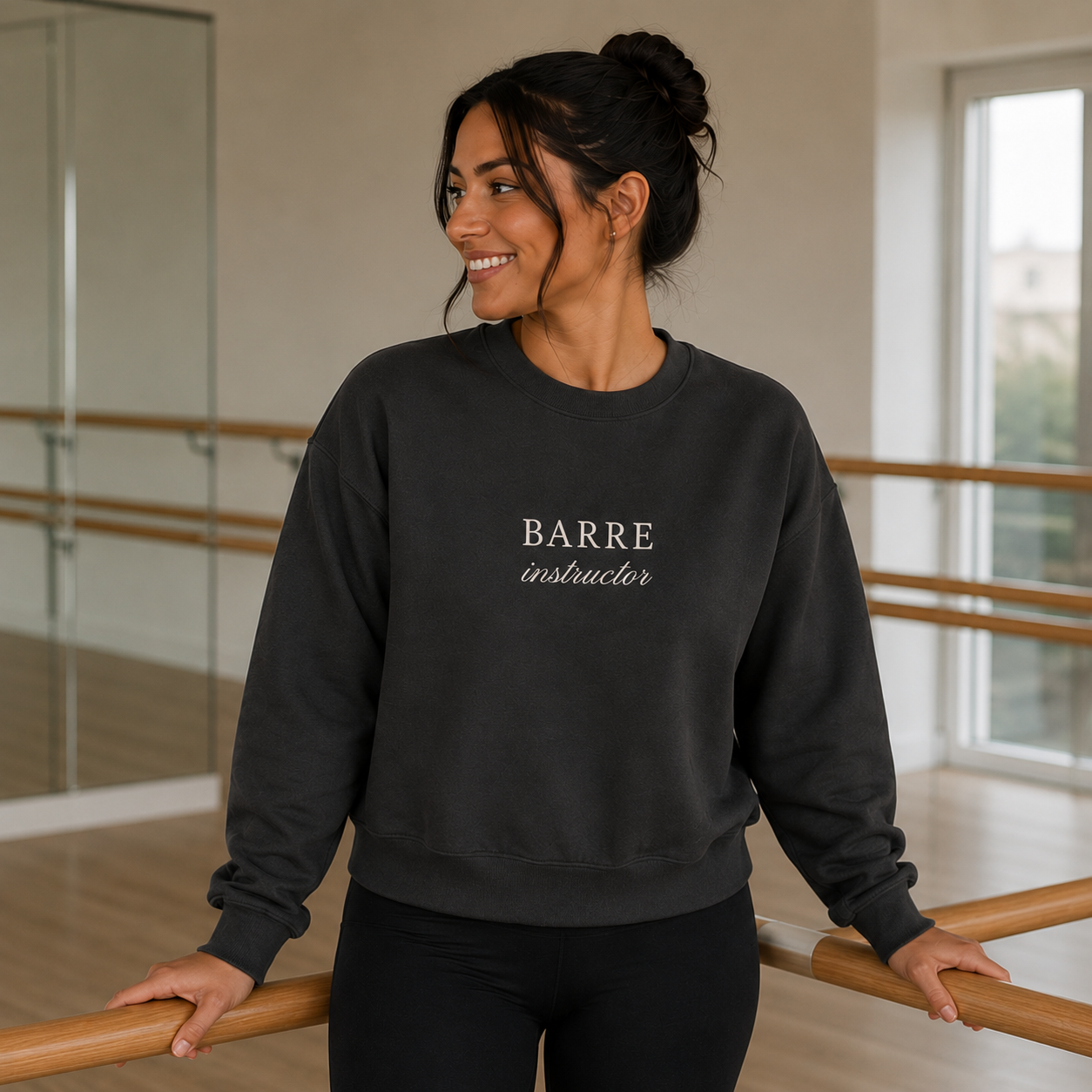 a woman is in a barre studio wearing an embroidered crewneck that says barre instructor on it