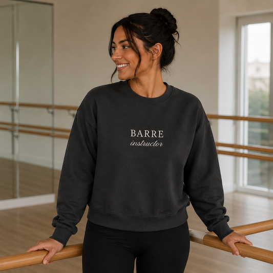 a woman is in a barre studio wearing an embroidered crewneck that says barre instructor on it