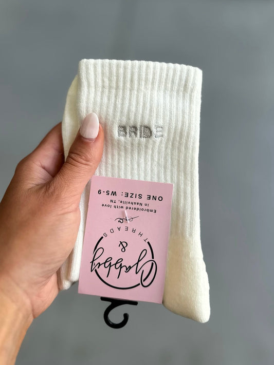 White socks with 'Bride' text held by a hand against a gray background