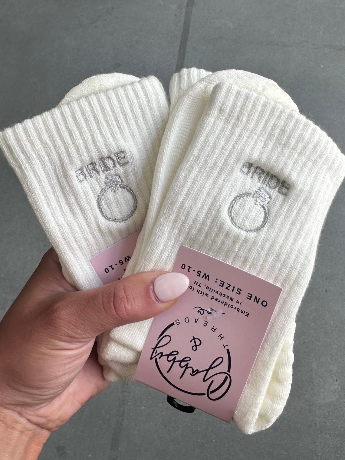 White socks with 'bride' and ring design held by a hand against a gray background