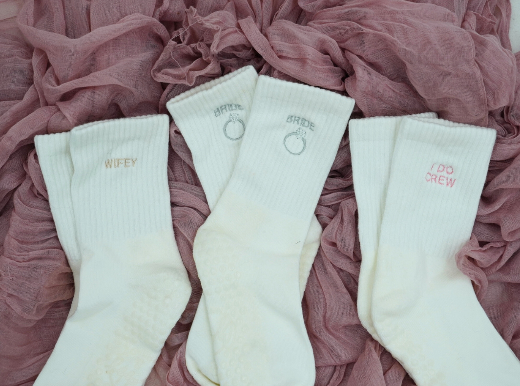 three pairs of socks laying on a pink textured background. each pair of pilates socks has a different bridal motif embroidered on it