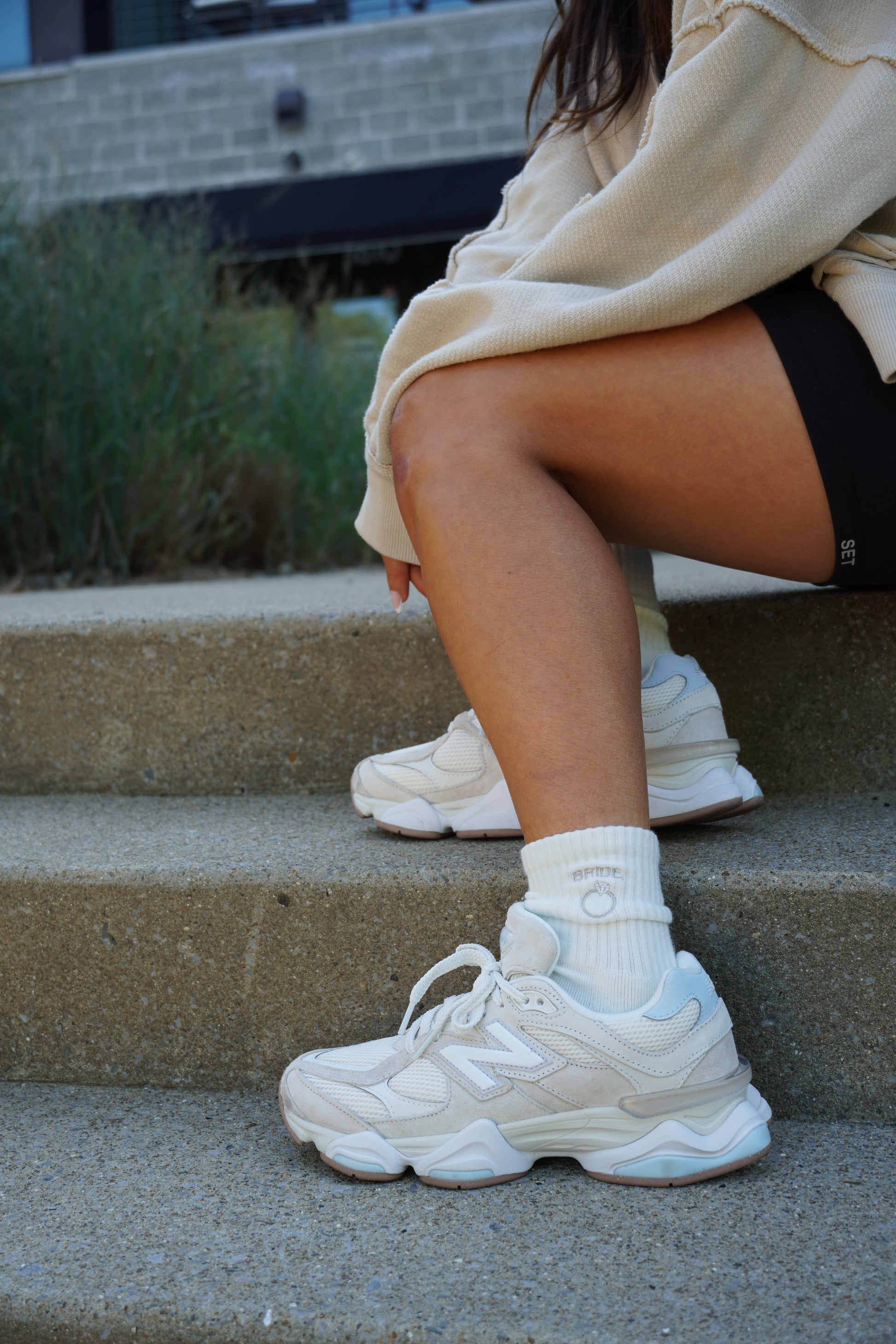 A person is sitting on a step wearing "Bride" embroidered crew socks with white sneakers