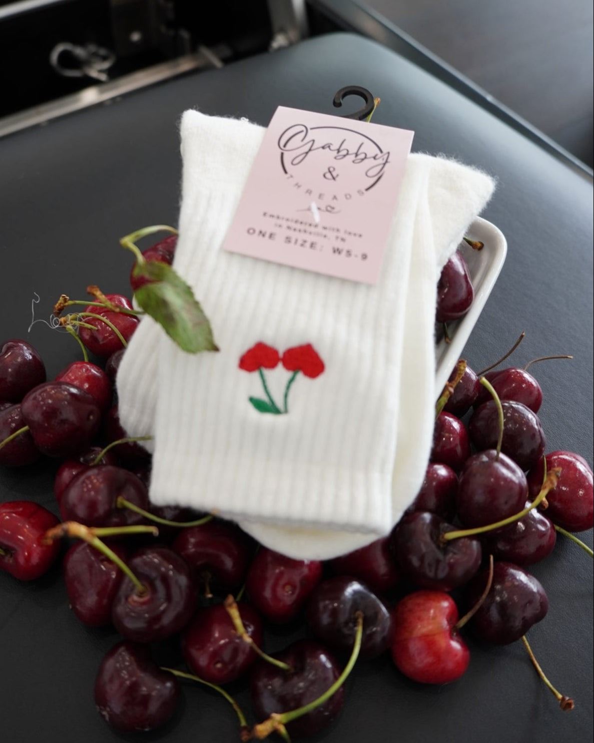 White socks with cherry heart embroidery design on a black surface with cherries