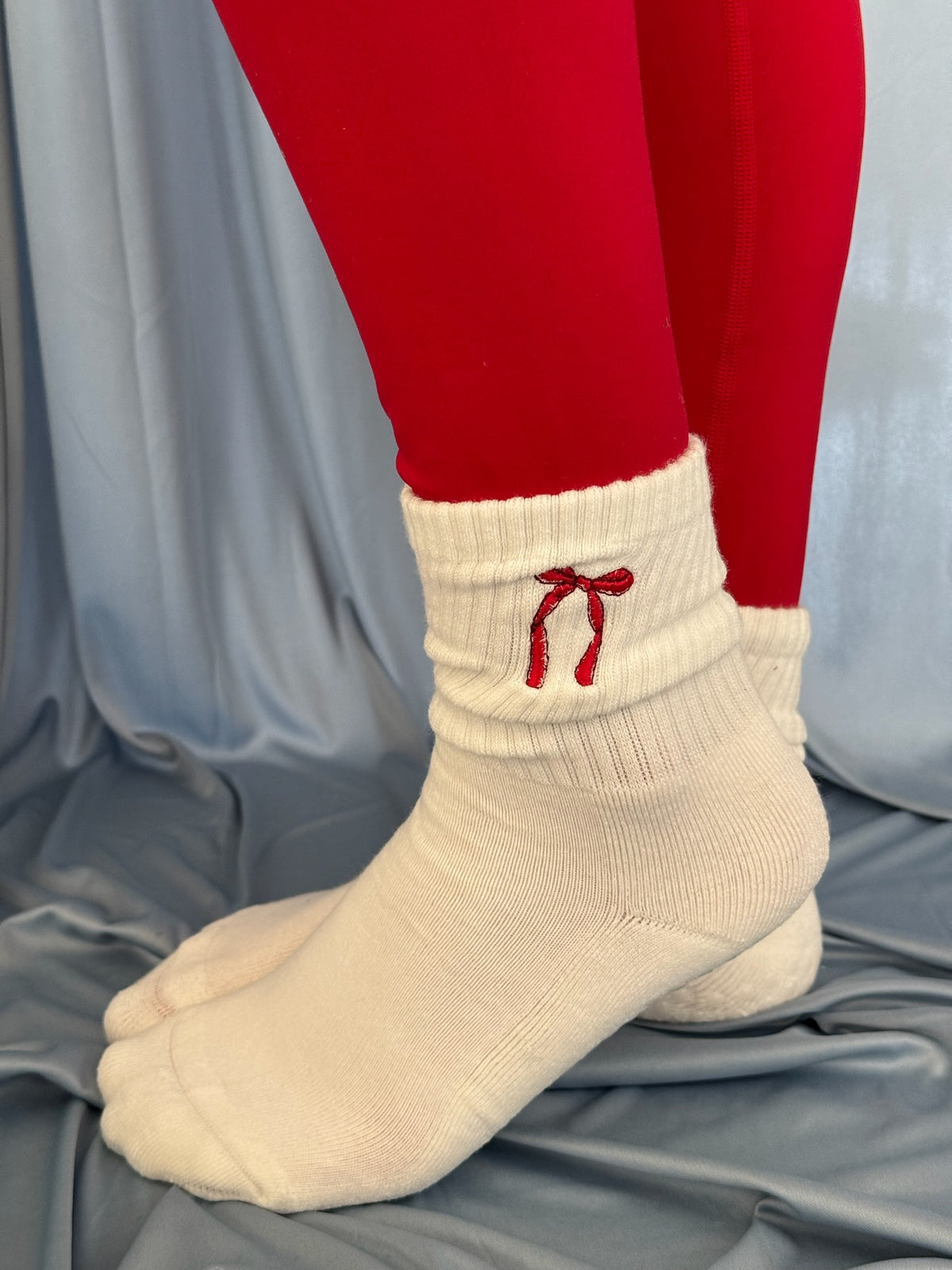 a person is wearing a pair of red leggings and a pair of white grip socks with red christmas coquette bows on them