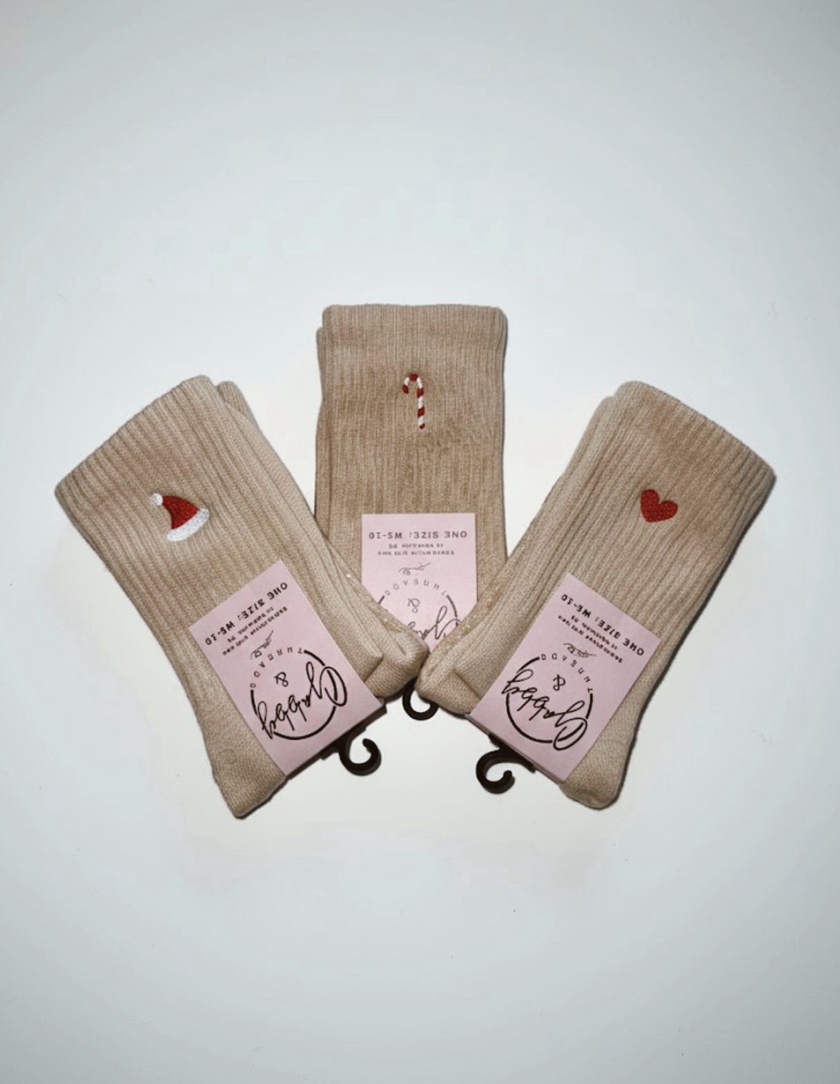 three pairs of beige grip socks featuring different christmas icons (santa hat, candy cane, and red heart)