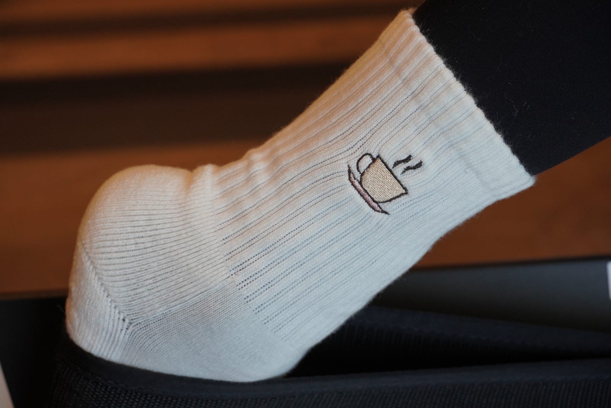 a person is wearing a pair of white grip socks with an embroidered coffee cup on a pilates reformer