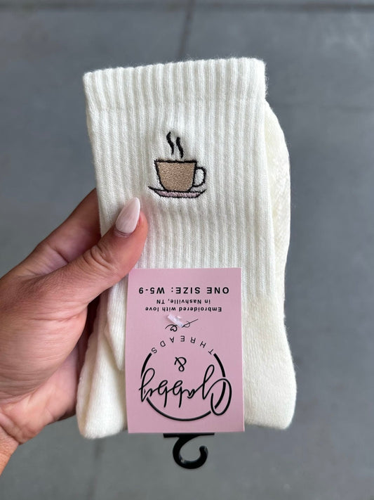 White socks with coffee cup design held by a hand against a gray background
