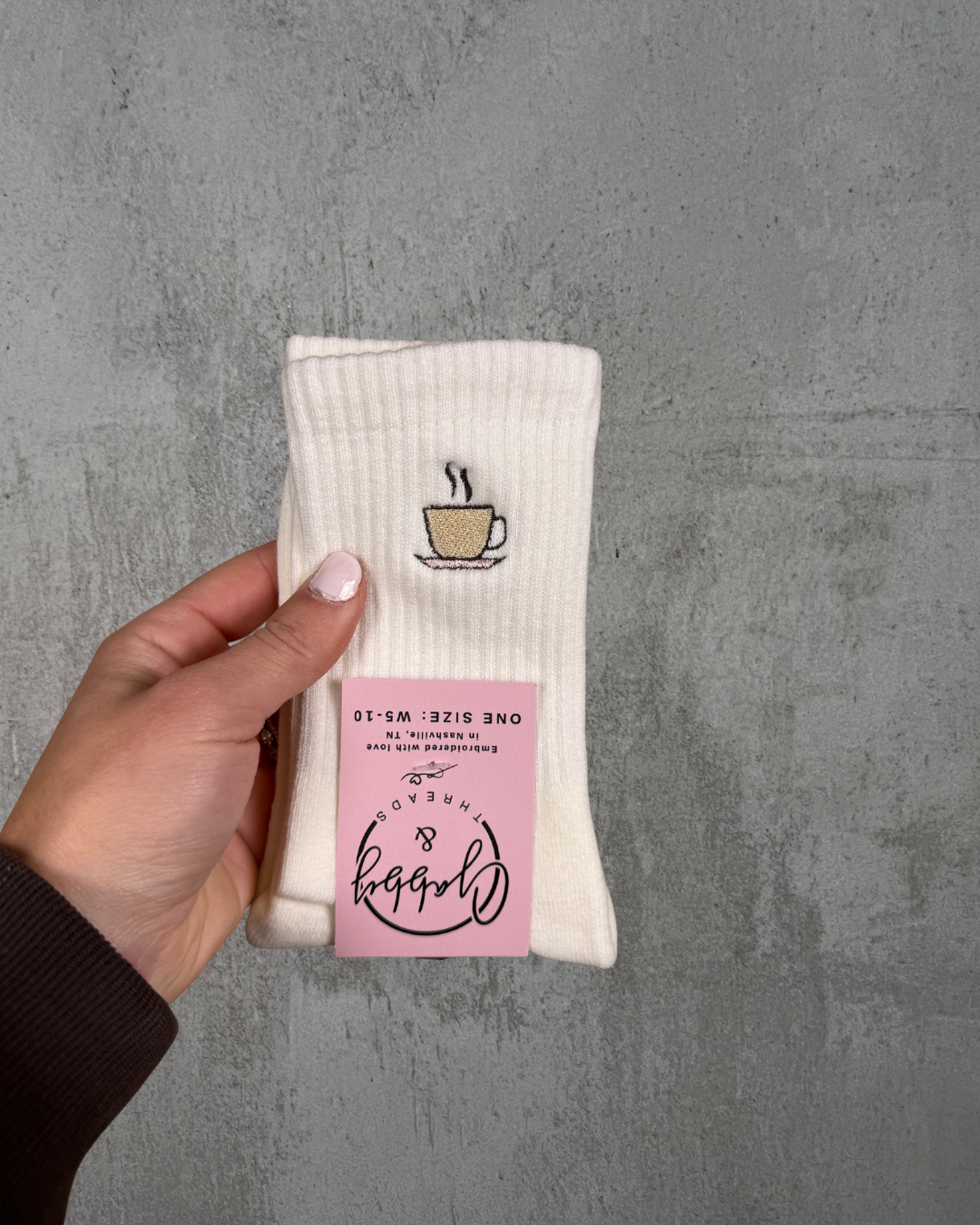 A pair of White grip socks with coffee cup design held by a hand against a gray background