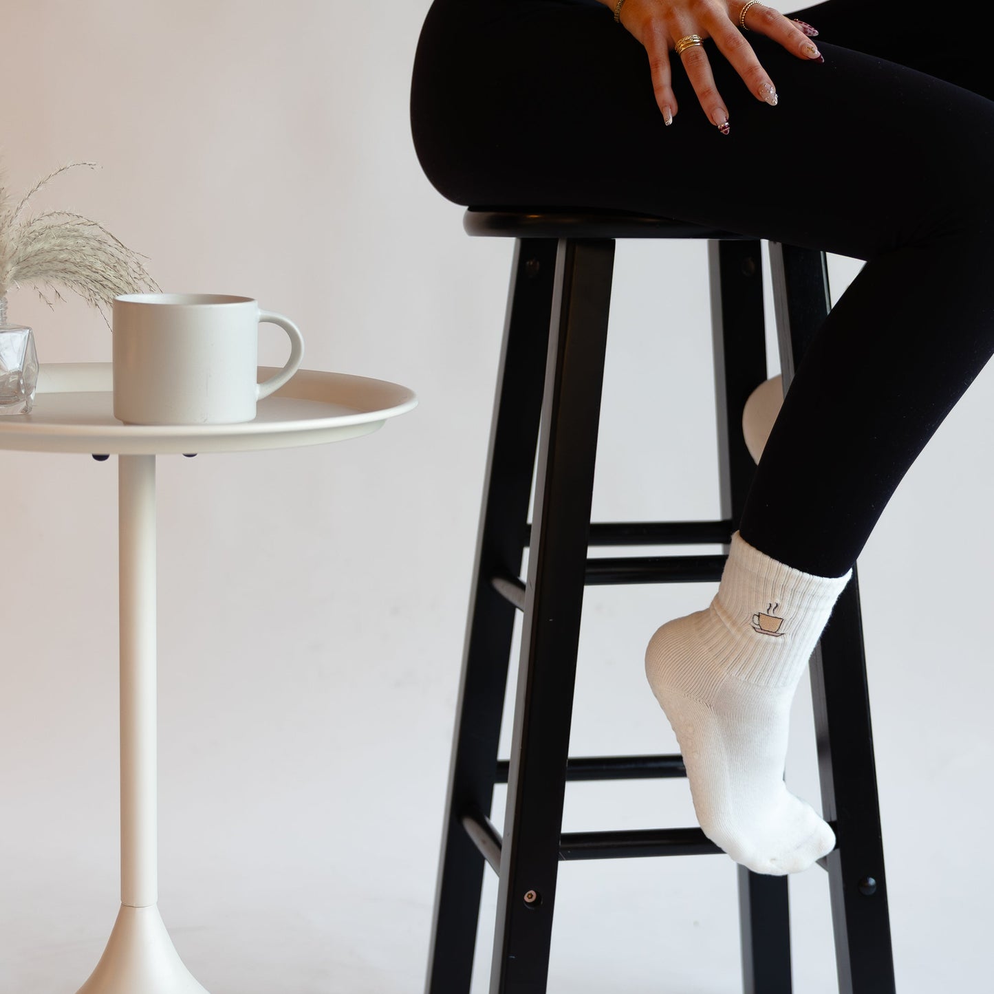 a person is sitting on a bar stool in a black activewear set wearing white grip socks with a coffee cup embroidered on them
