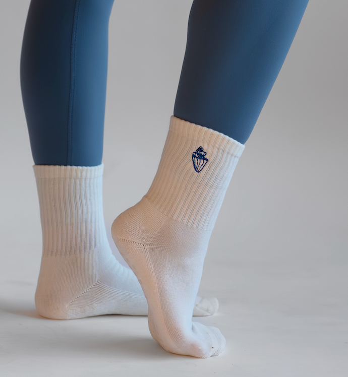 White socks with a  conch shell worn by a person in blue leggings on a light gray background