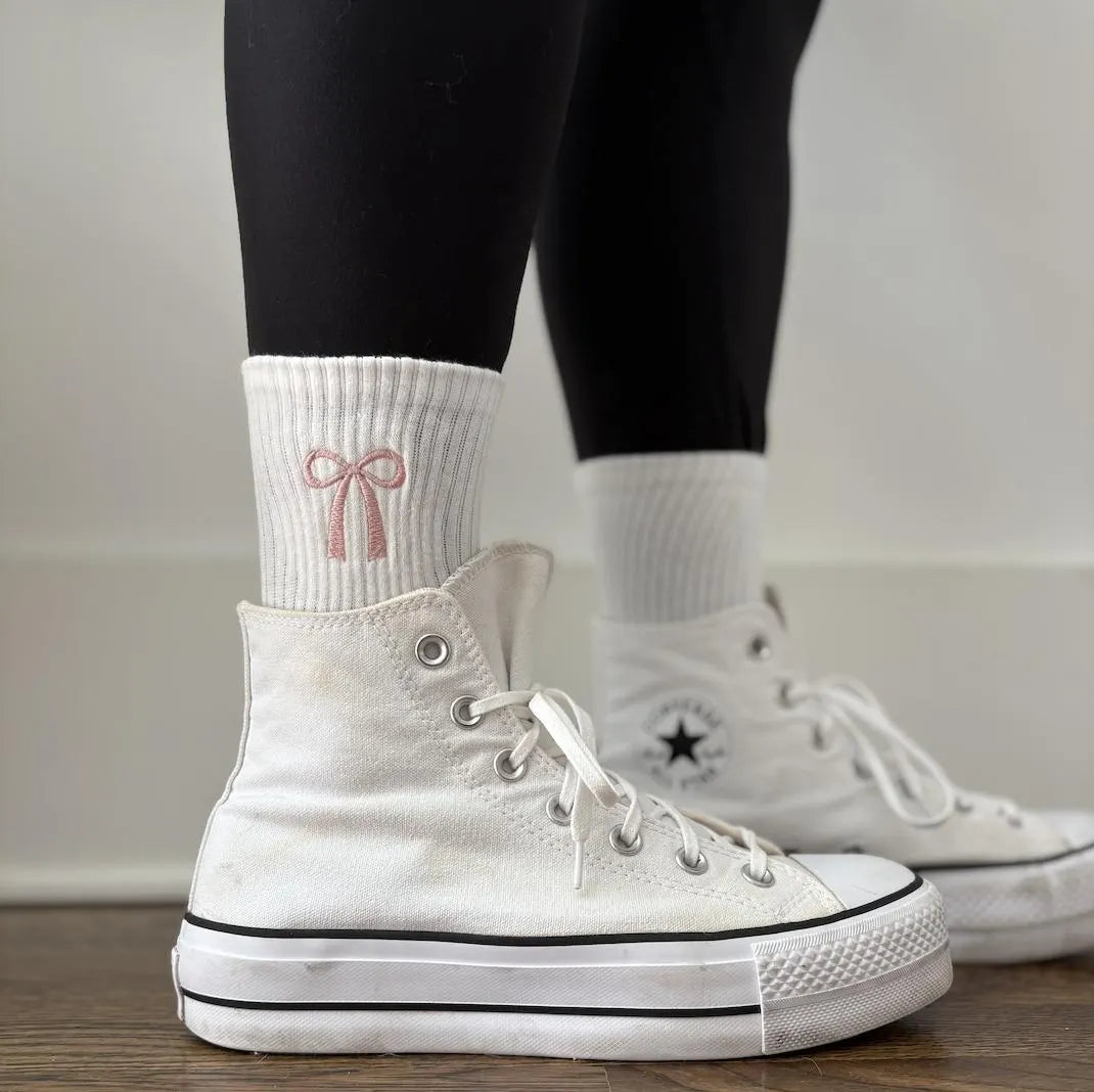 White high-top sneakers with black leggings with white socks featuring a pink bow design.