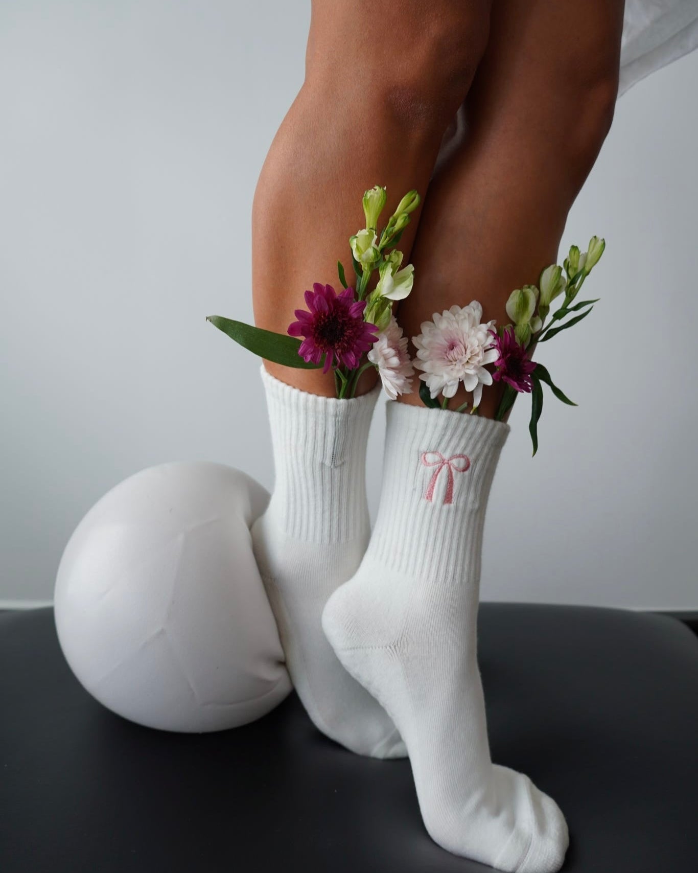 White socks featuring a pink coquette bow with floral arrangements held between them on a neutral background